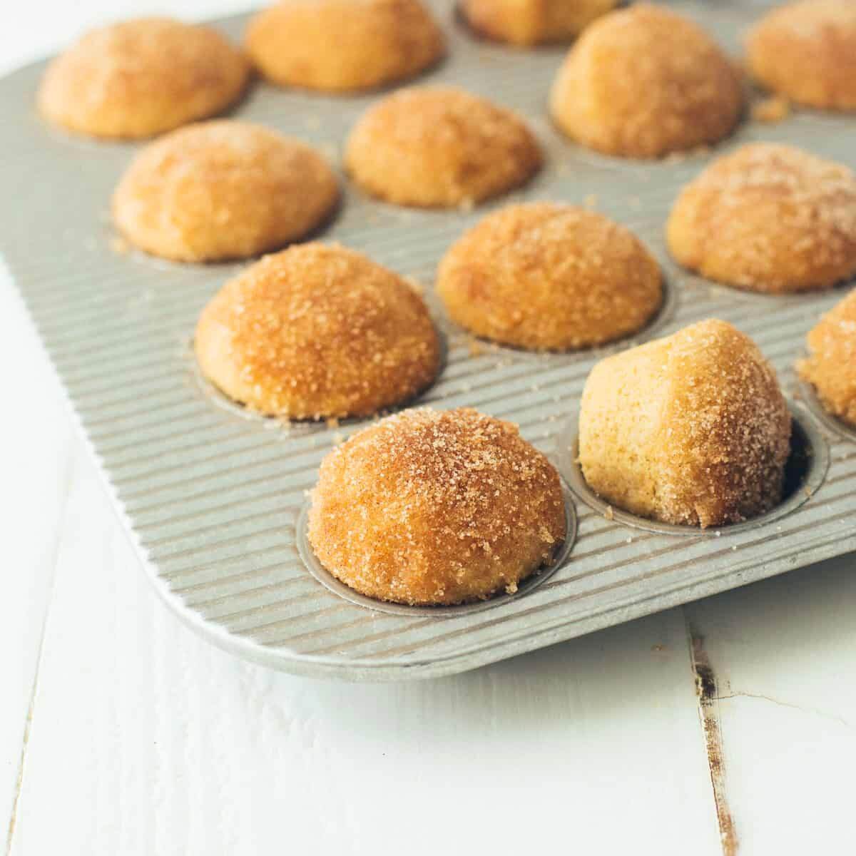 A muffin tin filled with baked apple cider donut mini muffins, coated in cinnamon sugar.