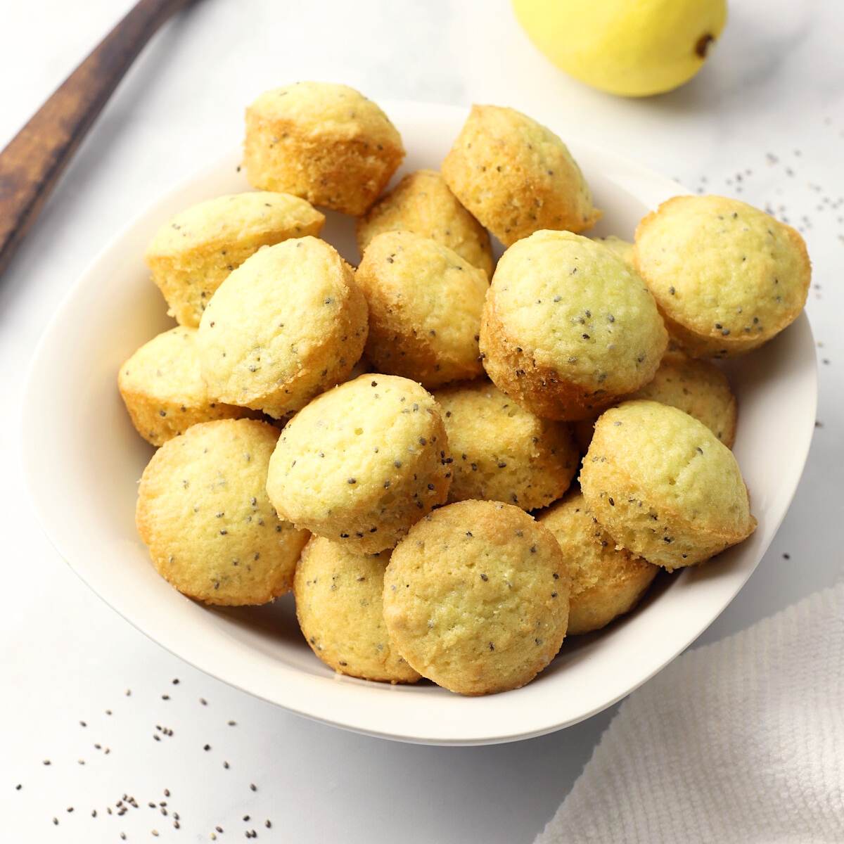 A bowl filled with mini lemon chia seed muffins, with a lemon in the background.