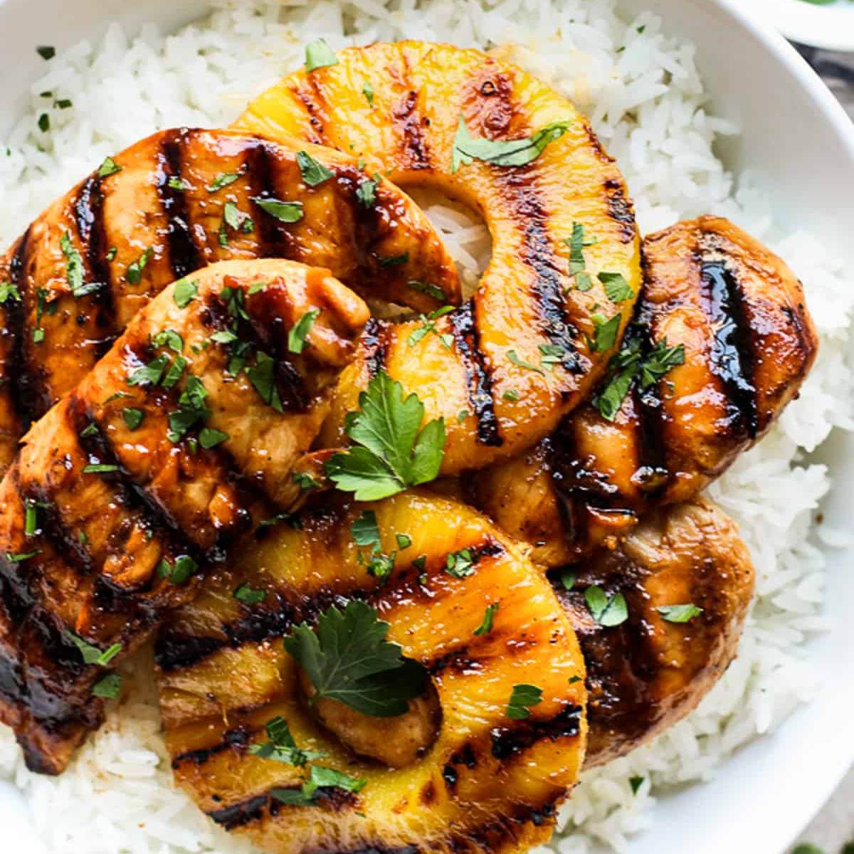 A bowl of grilled pineapple and chicken served over white rice. The chicken is glazed with a sweet and savory sauce and garnished with fresh parsley.