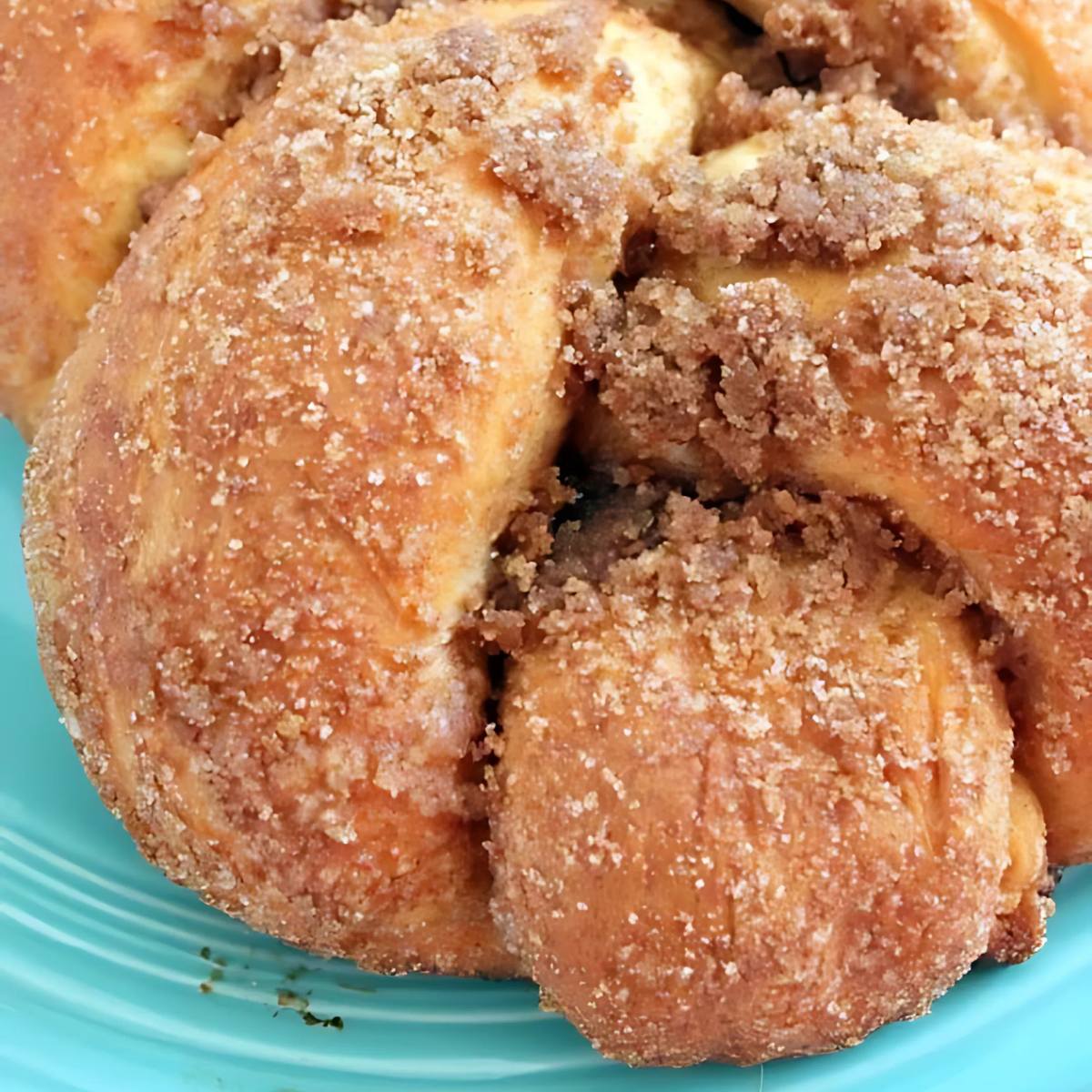 A close-up of a braided cinnamon roll with a golden-brown crust and a sprinkle of sugar.