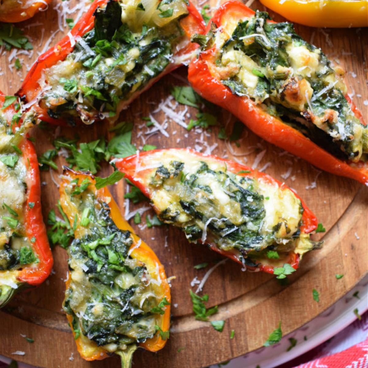 Baked mini peppers stuffed with spinach, feta cheese, and breadcrumbs, served on a wooden board.