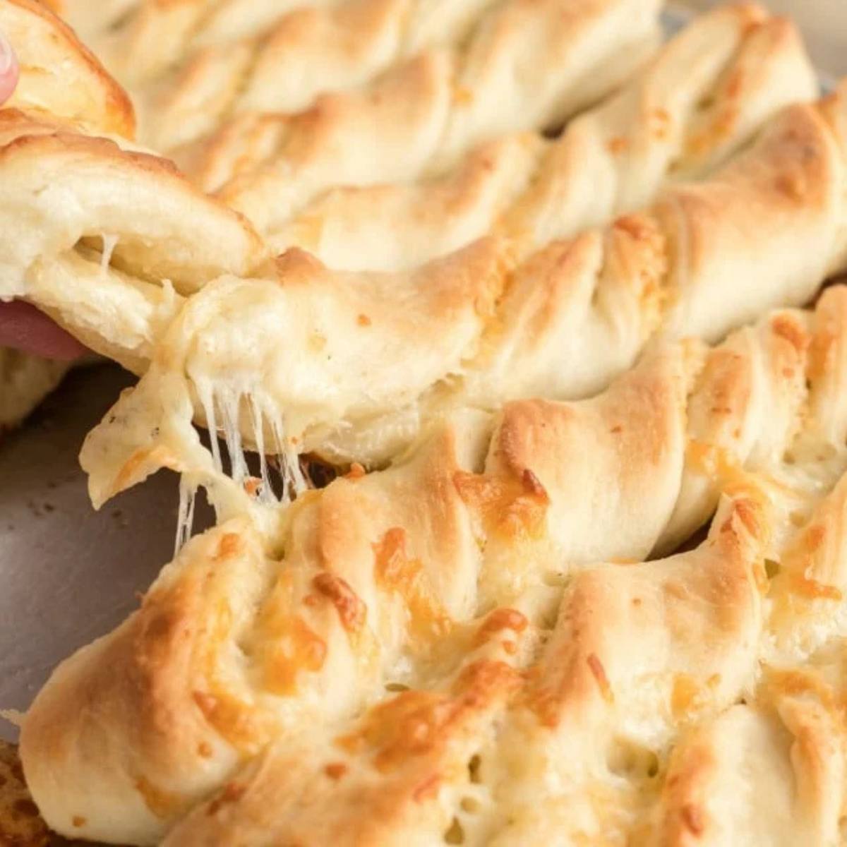 A hand pulling apart a golden-brown braided breadstick, revealing melted cheese inside.