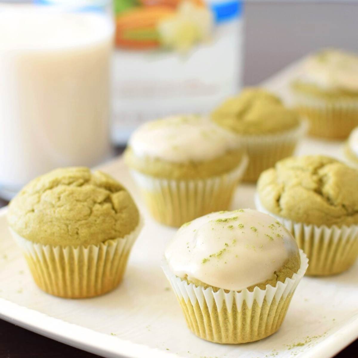 Matcha latte mini muffins with a white glaze, served on a plate with a glass of milk in the background.