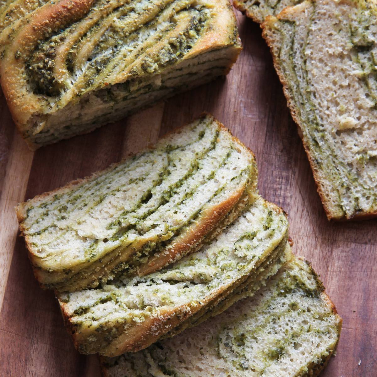 A loaf of bread with swirls of green pesto, sliced on a wooden cutting board.