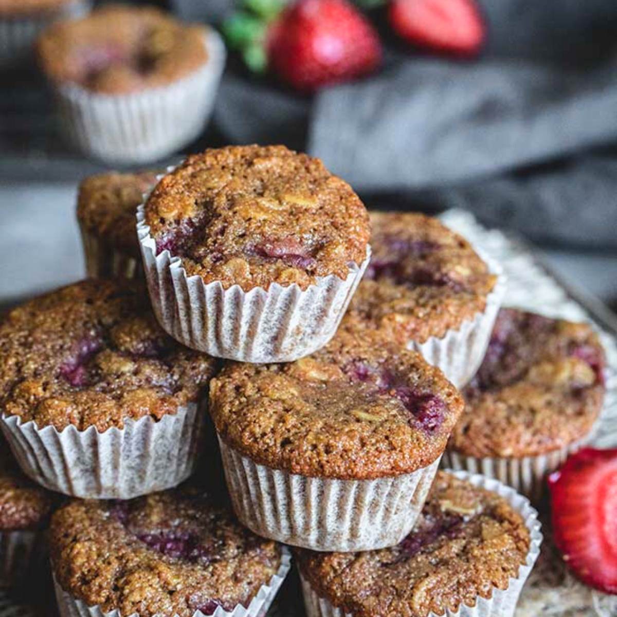 A pile of mini strawberry and raspberry muffins, with fresh strawberries in the background.