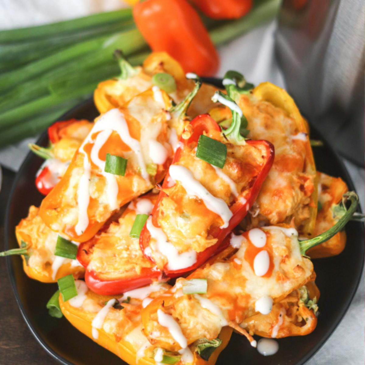  Baked mini peppers stuffed with buffalo chicken, cheese, and ranch dressing, topped with more ranch dressing and chopped green onions.