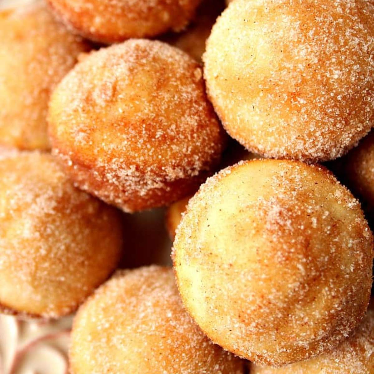 A close-up of cinnamon sugar mini donut muffins, coated in a sprinkled sugar.