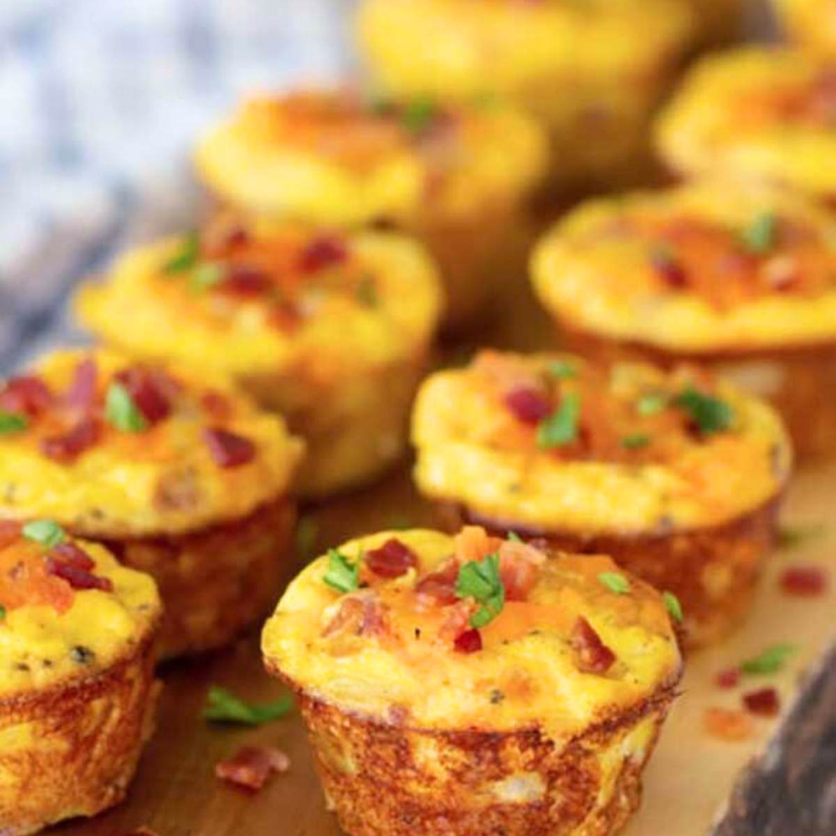 A row of mini egg muffins with bacon and cheese, garnished with fresh parsley.