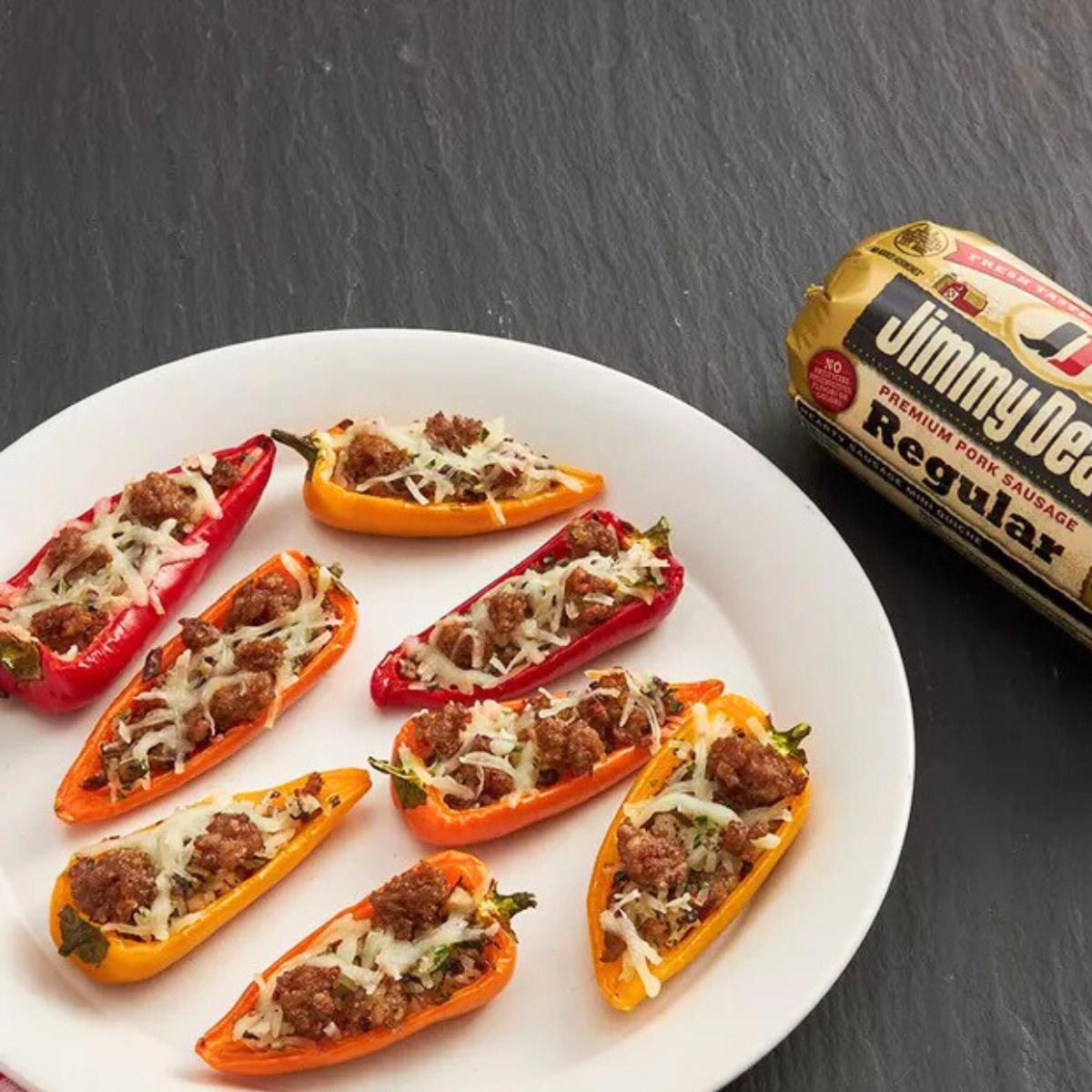 Baked mini peppers stuffed with Jimmy Dean sausage and cheese, served on a plate with a package of Jimmy Dean sausage in the background.