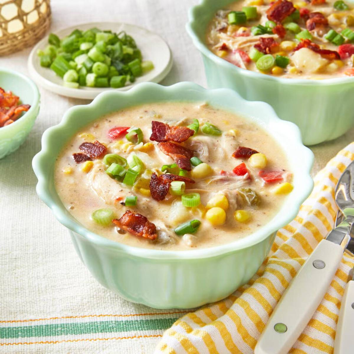 Two bowls of creamy chicken corn chowder, topped with crumbled bacon and chopped green onions. The soup contains visible chunks of chicken, corn, potatoes, and red peppers.