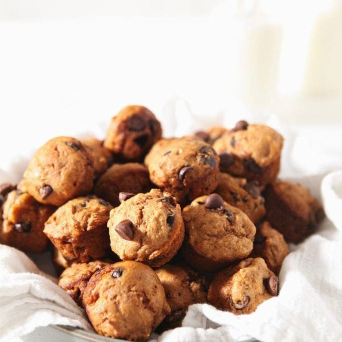 A pile of mini pumpkin chocolate chip muffins on a white cloth.