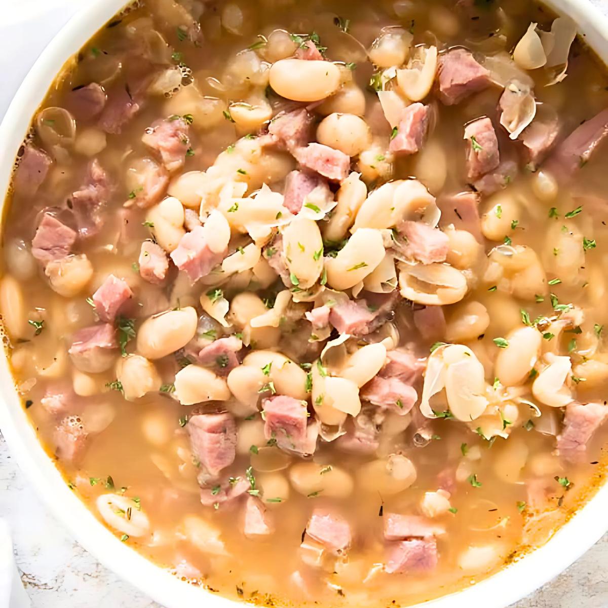 A bowl of creamy ham and white bean soup, filled with chunks of ham and tender white beans. The soup is a light brown color and is topped with fresh parsley.