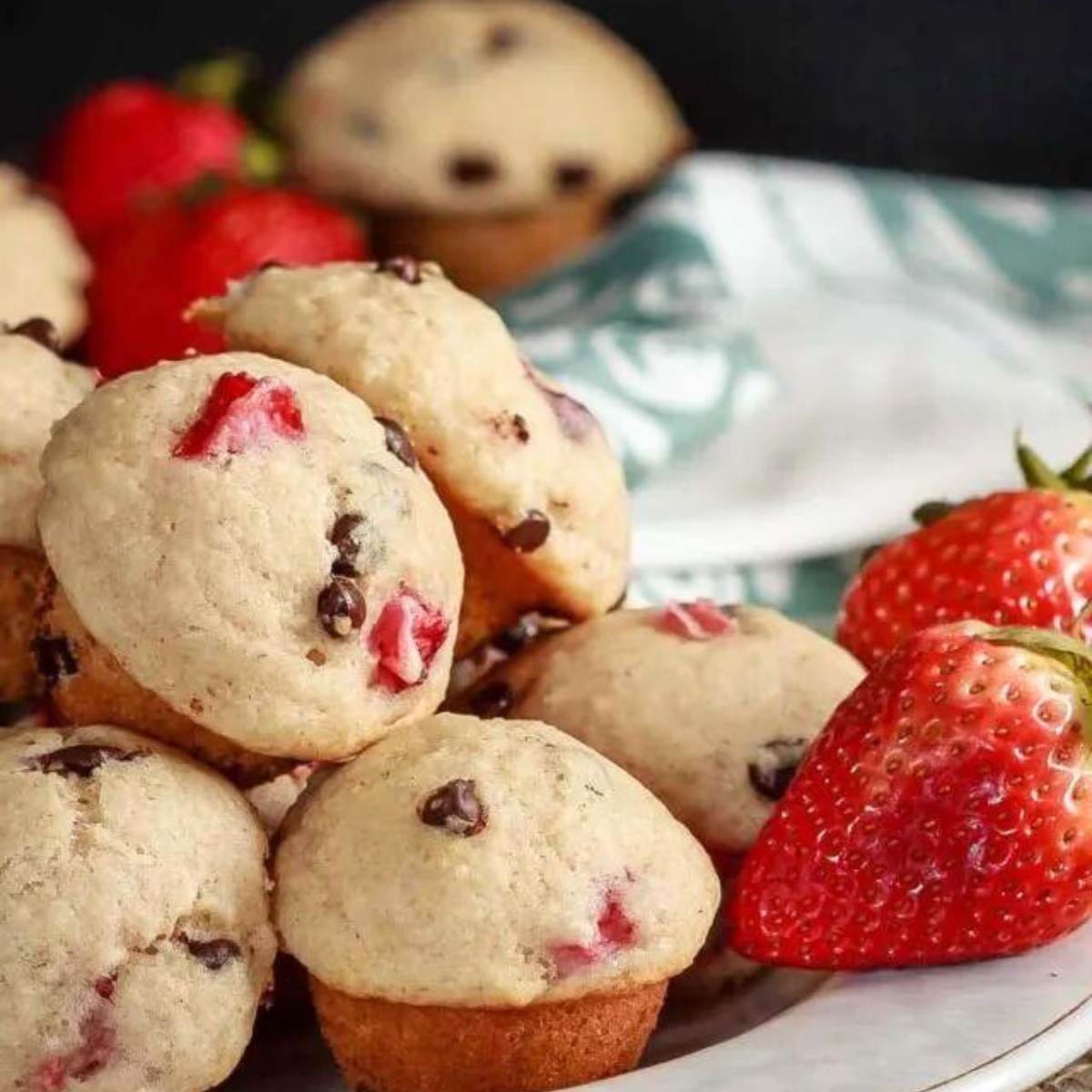 A plate of mini strawberry chocolate chip muffins, with fresh strawberries on the side.