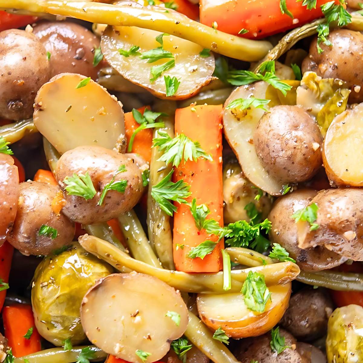 A close-up of roasted fall vegetables, including potatoes, carrots, green beans, and Brussels sprouts. The vegetables are seasoned and lightly browned, with fresh parsley sprinkled on top.