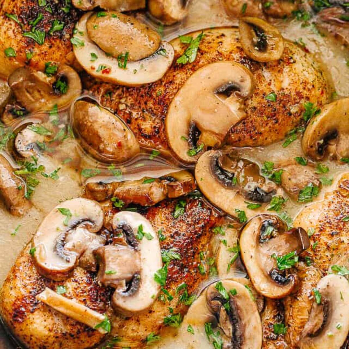 A close-up photo of chicken breasts cooked in a creamy mushroom sauce. The chicken is browned and the mushrooms are sautéed. Fresh parsley is sprinkled on top.