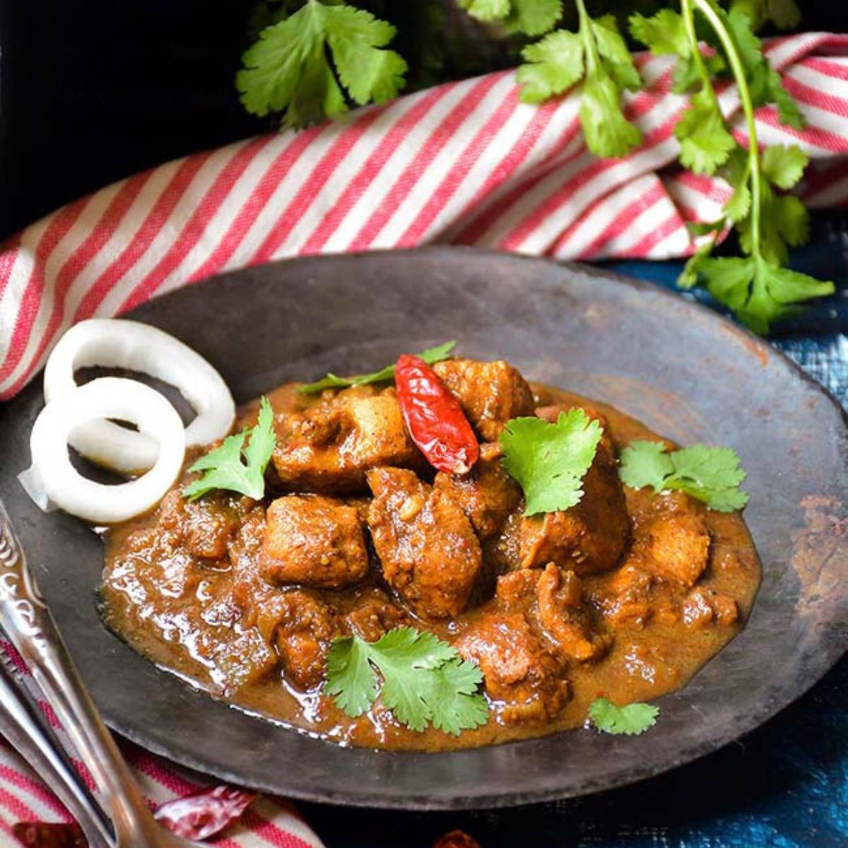  A plate of chicken vindaloo, a spicy Indian curry dish, garnished with fresh cilantro, red chili peppers, and onion slices.