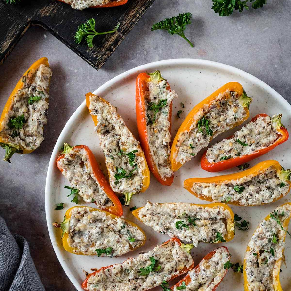 Baked mini peppers stuffed with a creamy mushroom and cheese mixture, garnished with fresh parsley. Served on a white plate.