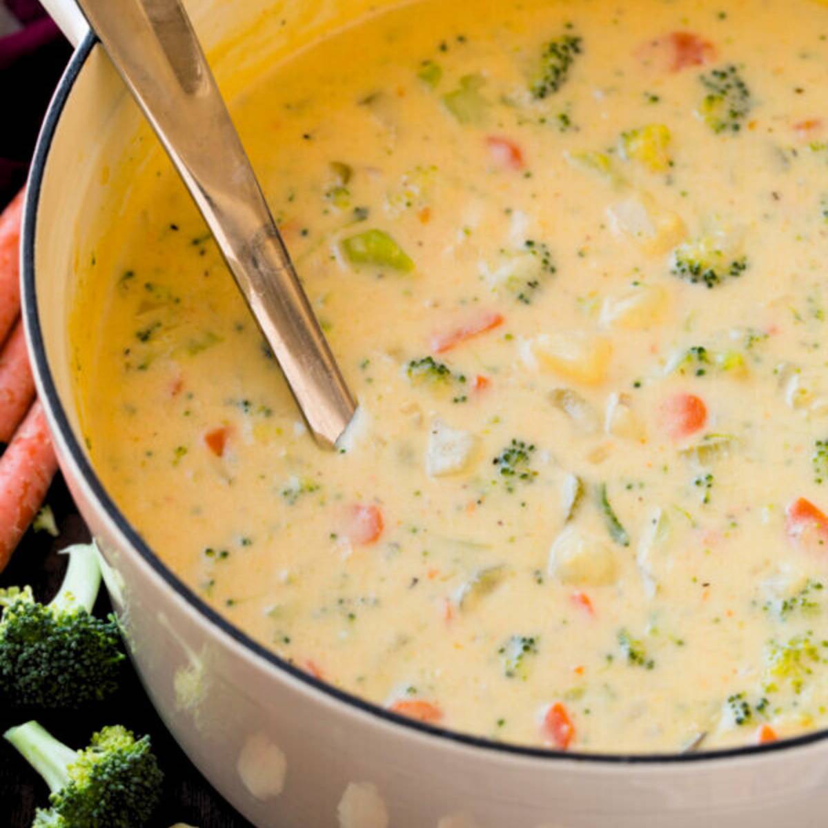  A large pot filled with creamy cheddar broccoli potato soup, with visible chunks of broccoli, carrots, and potatoes.