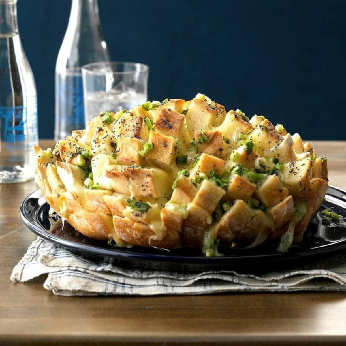 A golden-brown, cheesy pull-apart bread loaf, filled with melted cheese and green onions, resting on a blue plate.