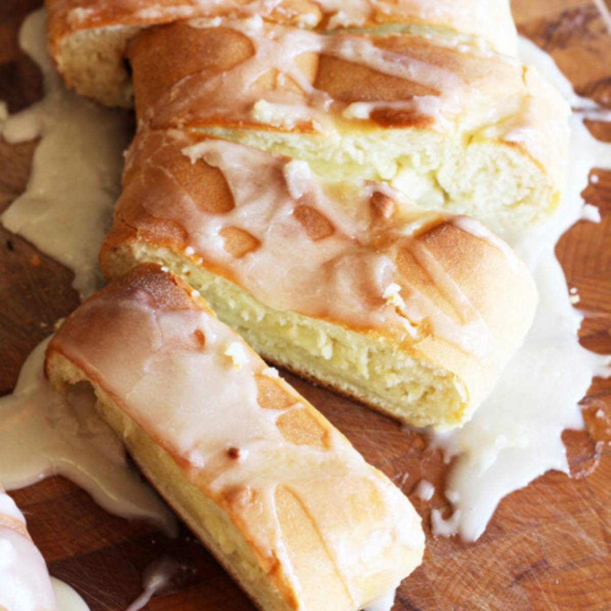 A golden-brown, glazed loaf of sweet bread with a creamy filling, partially sliced on a wooden board.