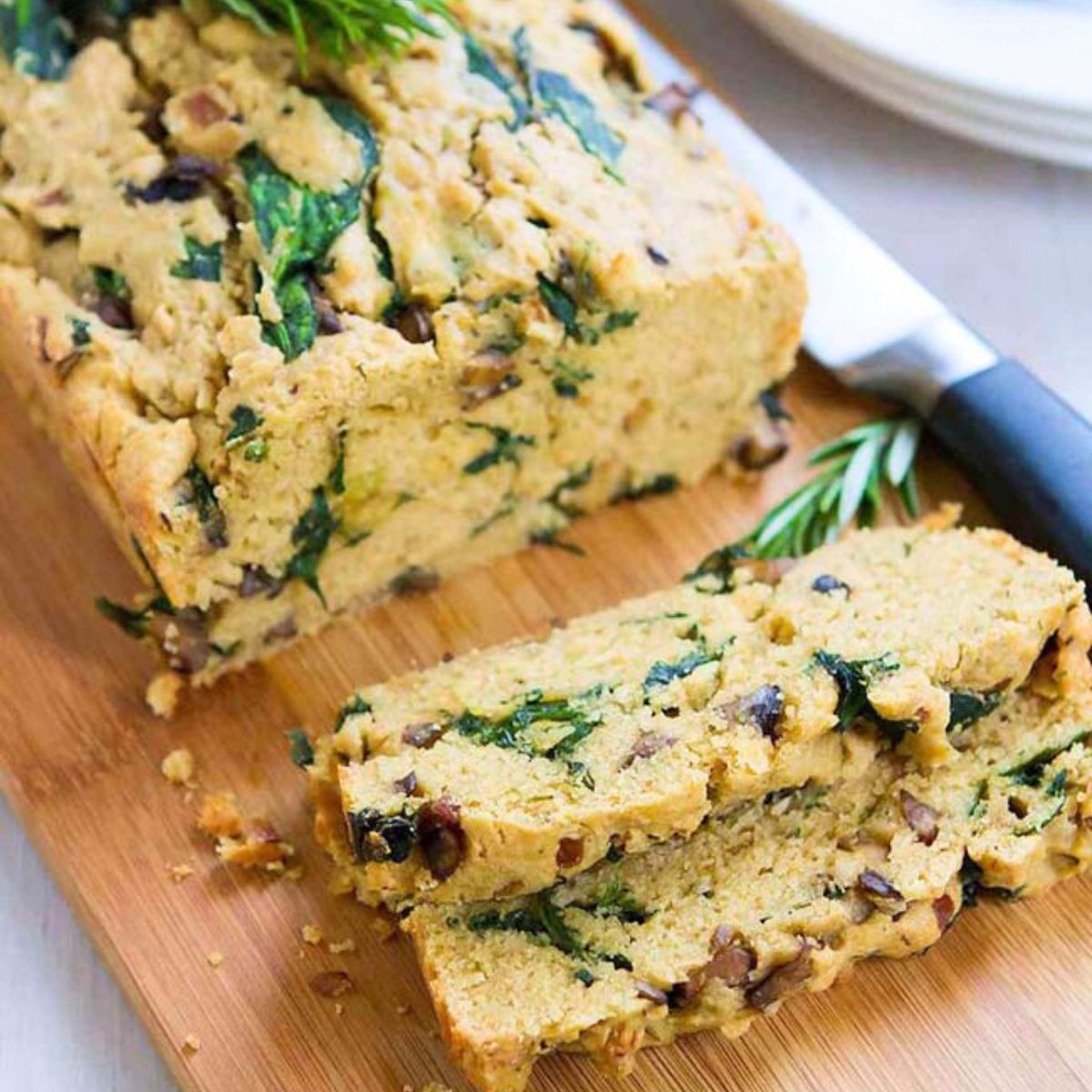 A loaf of savory bread, sliced and filled with mushrooms and spinach, on a wooden cutting board.