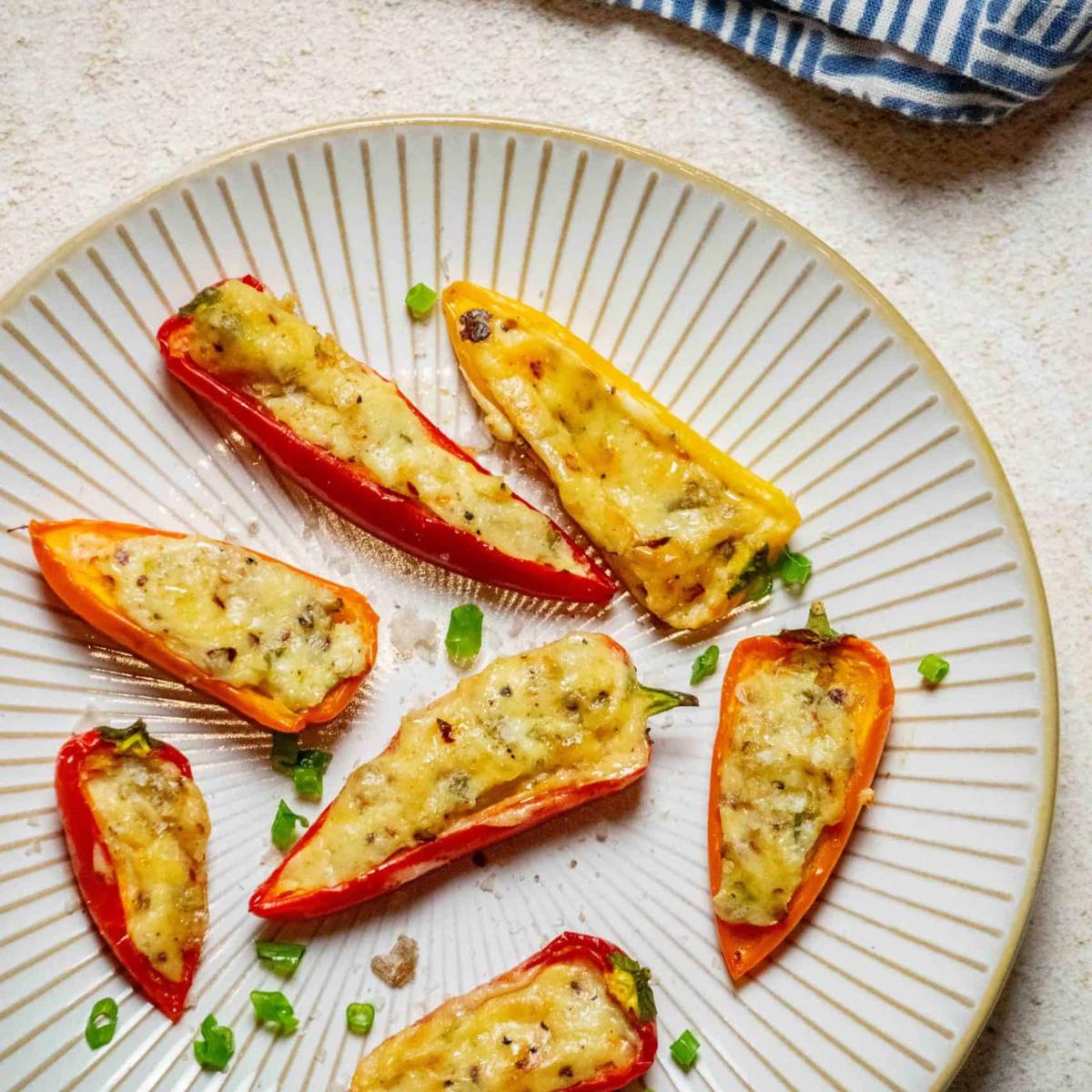 Baked mini peppers stuffed with cheese and herbs, served on a plate with chopped green onions.