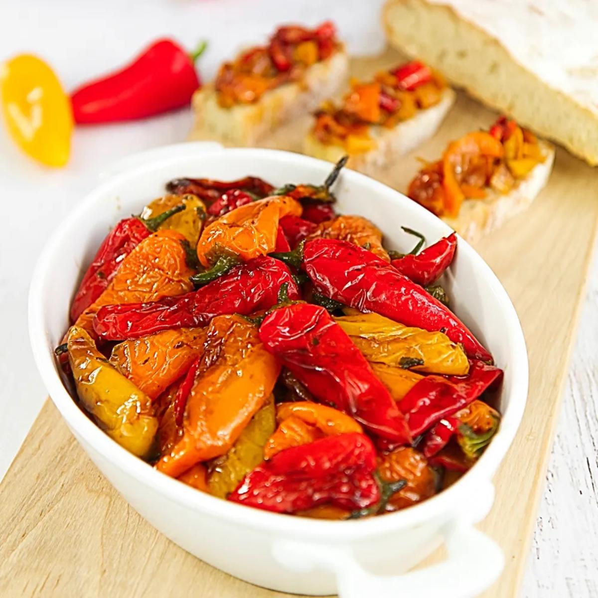 Roasted red and yellow mini peppers in a white dish, served with toasted bread.