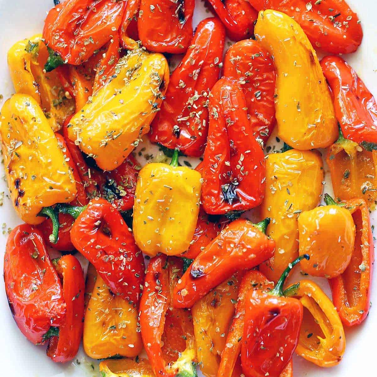 Roasted red and yellow mini peppers seasoned with herbs, served on a white plate.