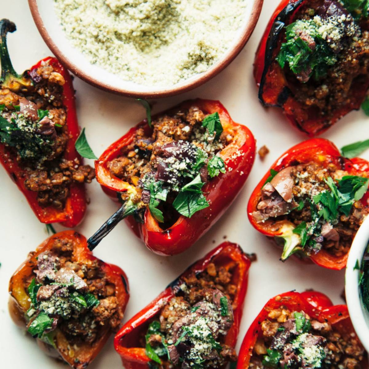 Baked stuffed mini peppers with a meat and vegetable filling, topped with olives, herbs, and a sprinkle of breadcrumbs.