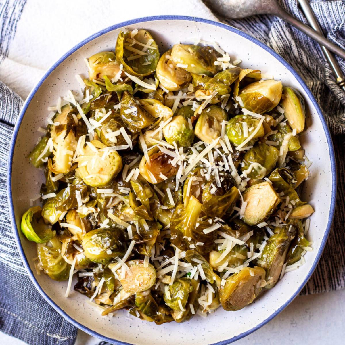 A bowl of roasted Brussels sprouts, tossed with bacon and Parmesan cheese. The sprouts are browned and slightly charred, with some leaves still intact. 