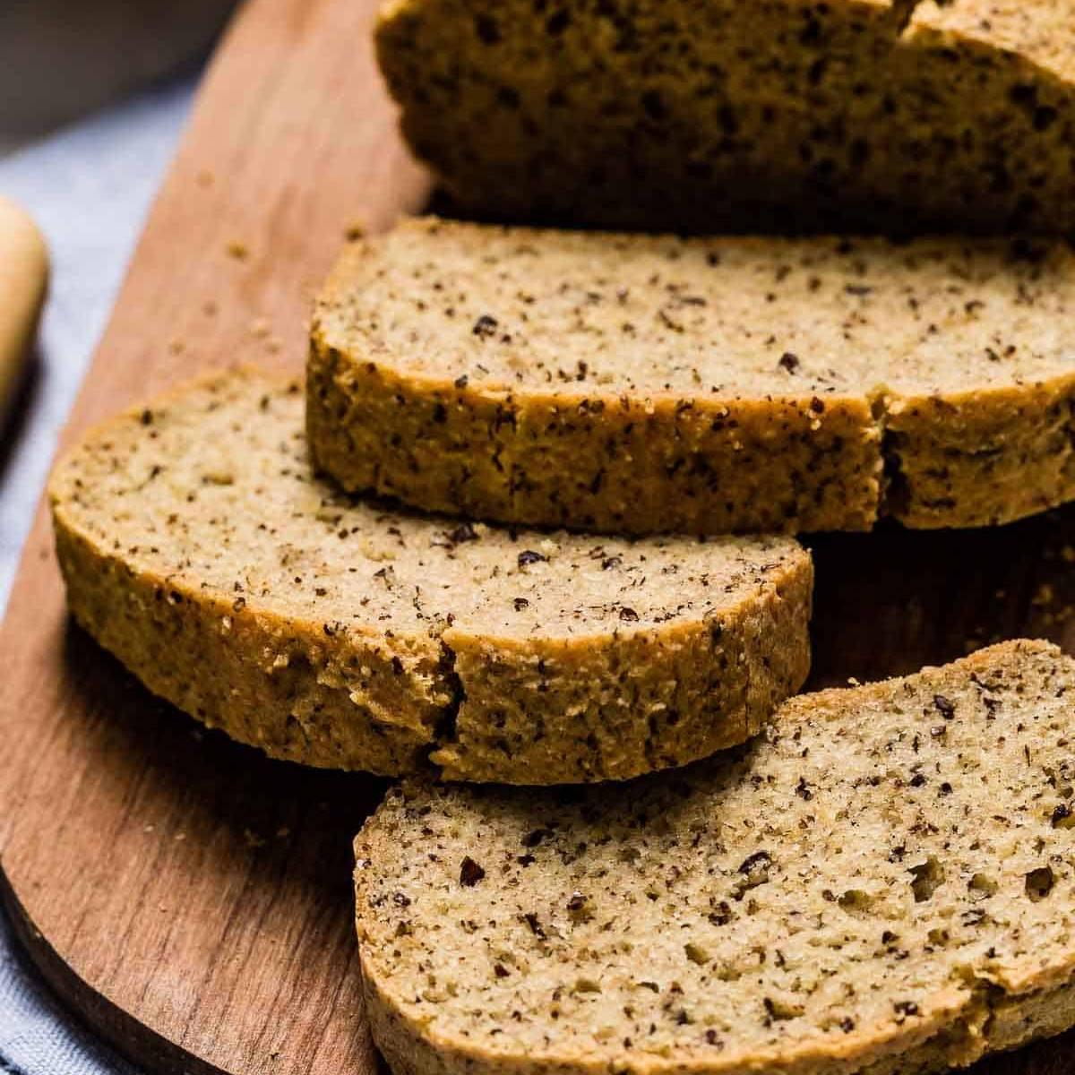 A loaf of dark, crusty bread with dried fruit and nuts, sliced in half on a white surface.