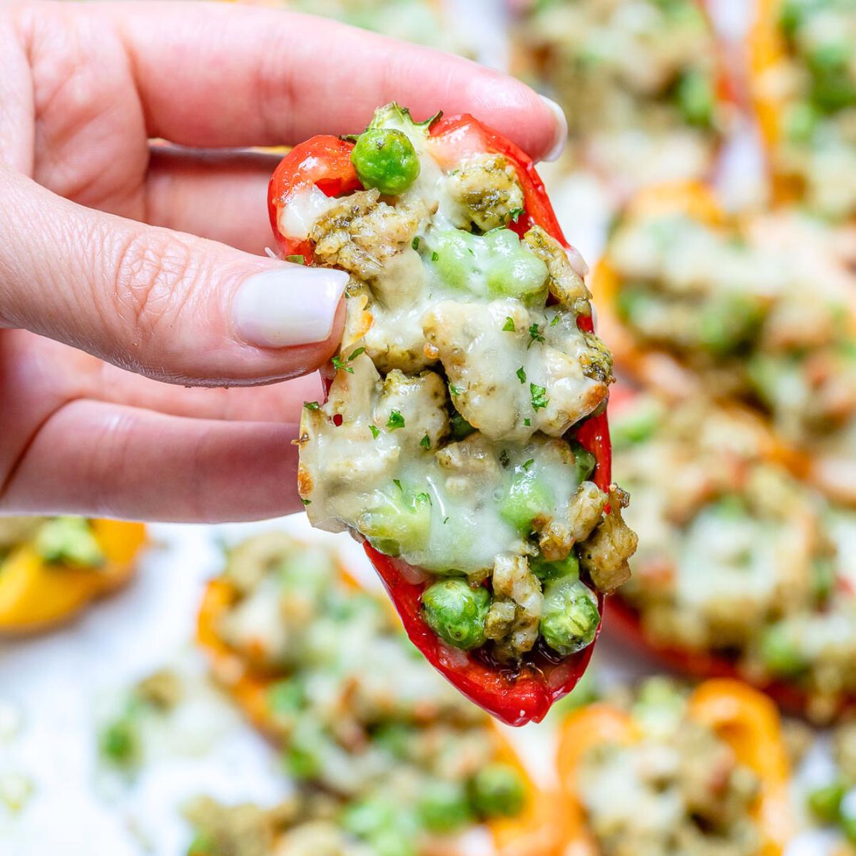  A close-up of a hand holding a stuffed mini pepper filled with a creamy pesto and chicken mixture with peas.