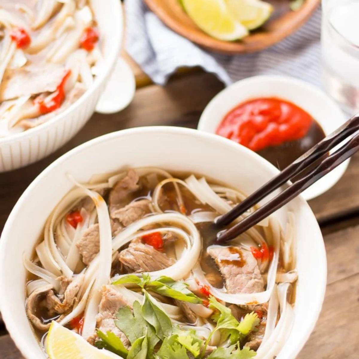  Two bowls of pho, a Vietnamese noodle soup. The soup contains rice noodles, thinly sliced beef, herbs, and a flavorful broth. Sliced red chili peppers are floating in the broth. 