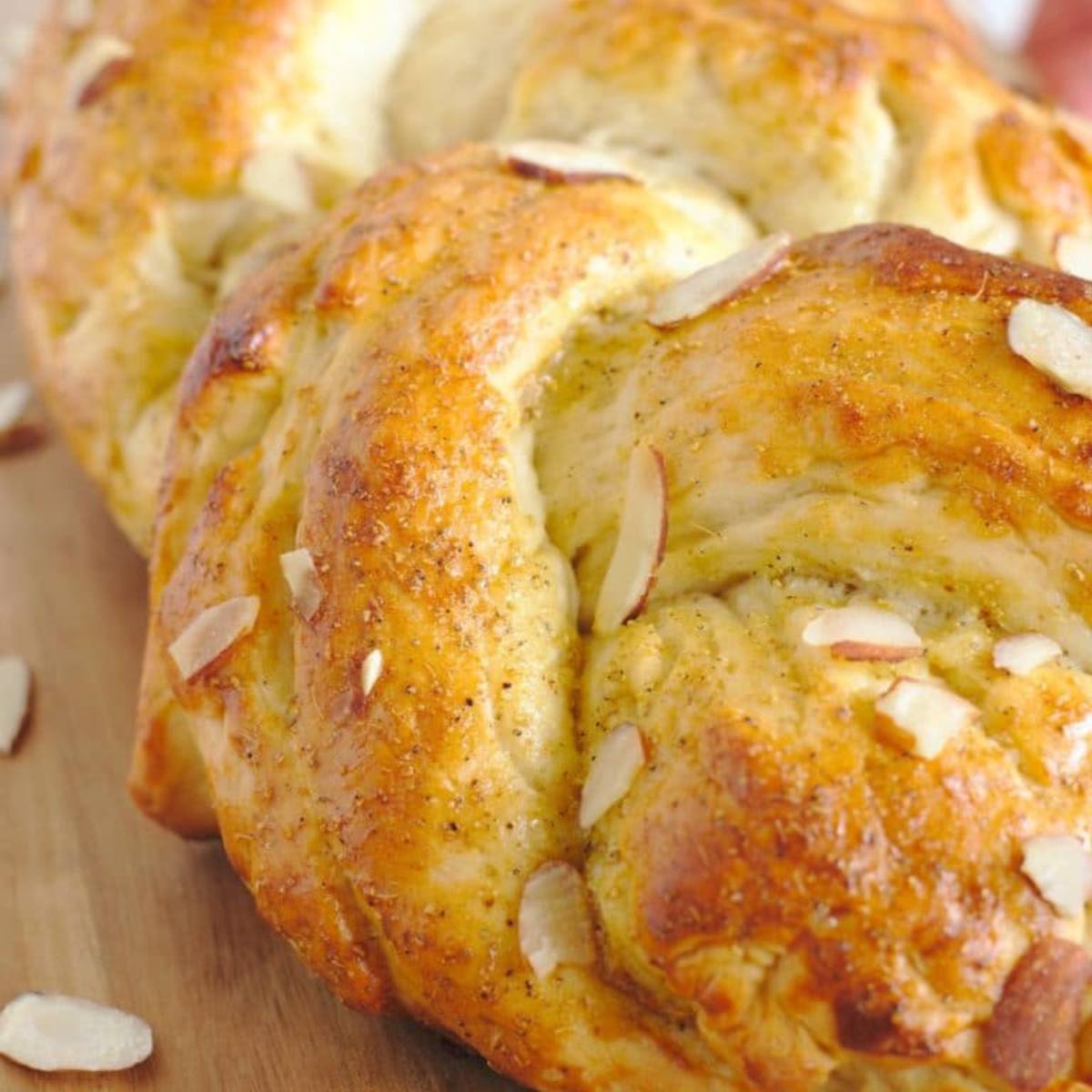 A golden-brown braided loaf of bread topped with sliced almonds.