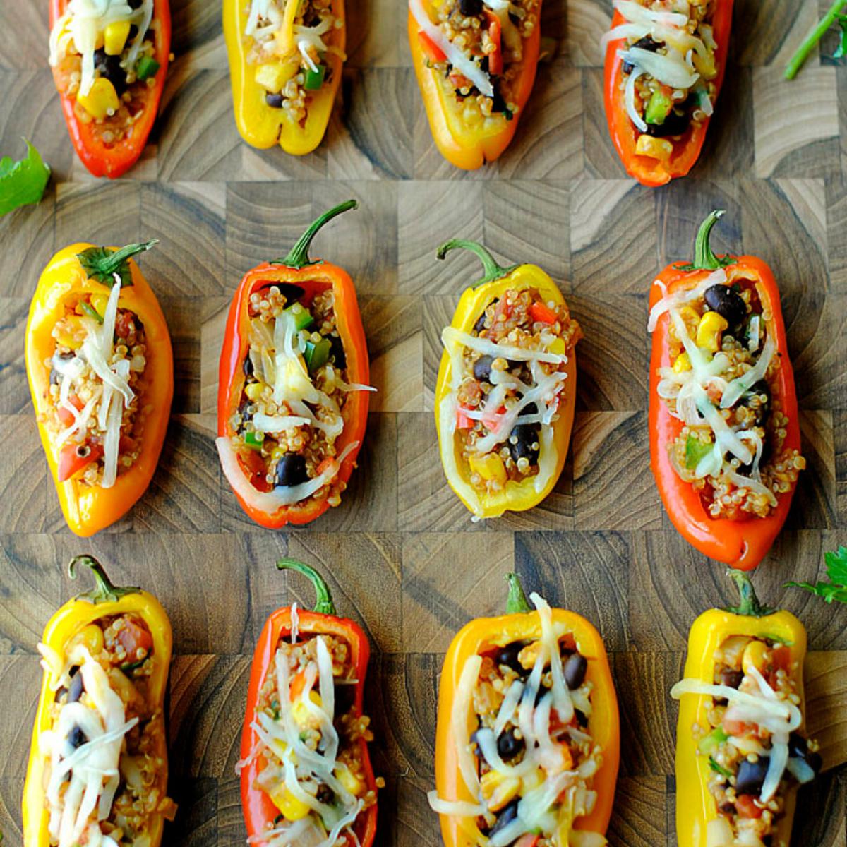 Baked mini peppers stuffed with a quinoa and vegetable mixture, topped with cheese. Served on a wooden cutting board.