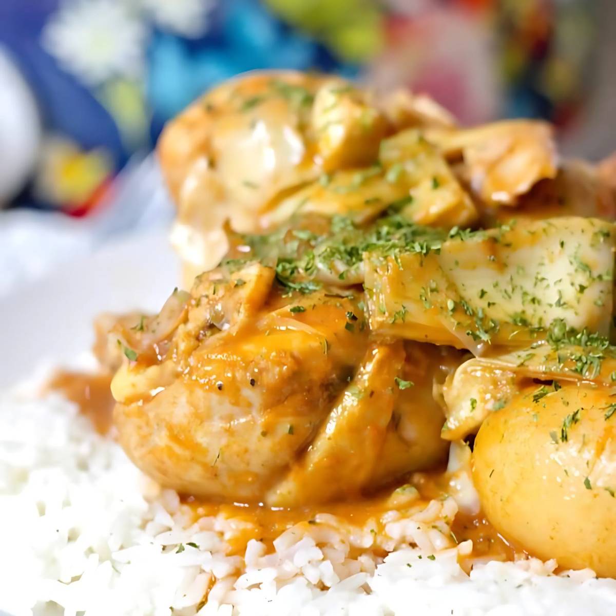 A close-up photo of chicken adobo served over a bed of white rice. The chicken is braised in a tangy vinegar-based sauce and garnished with fresh parsley.