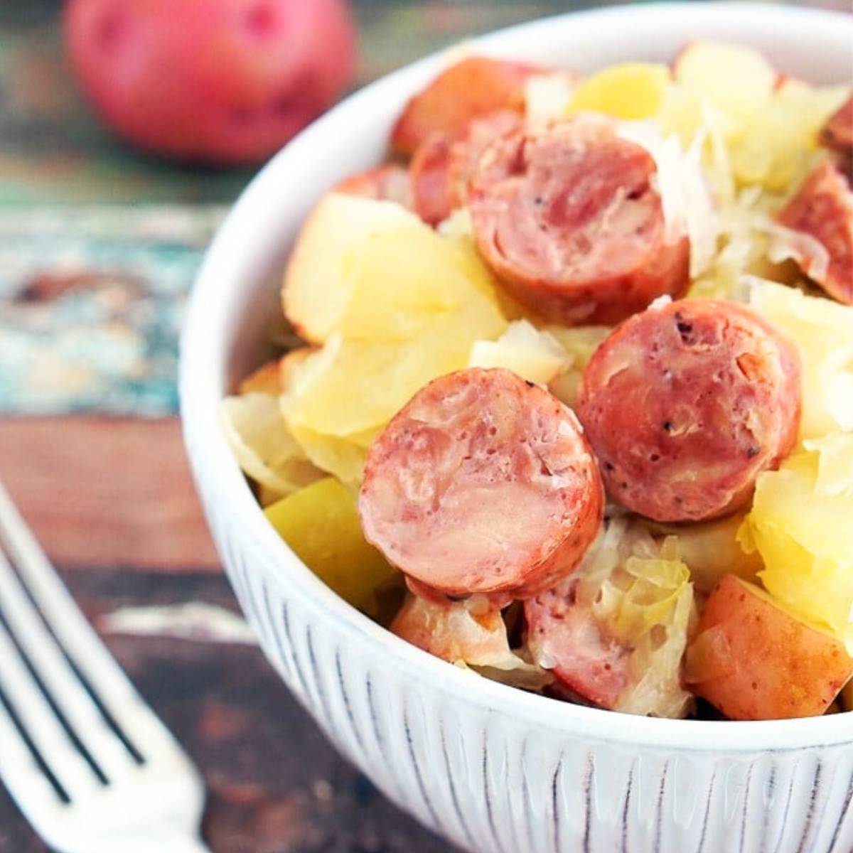 A bowl of sauerkraut and potatoes with sliced kielbasa sausage. Apples are also mixed in.