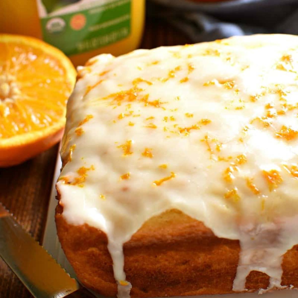 A golden-brown loaf of orange bread topped with a white glaze and orange zest.