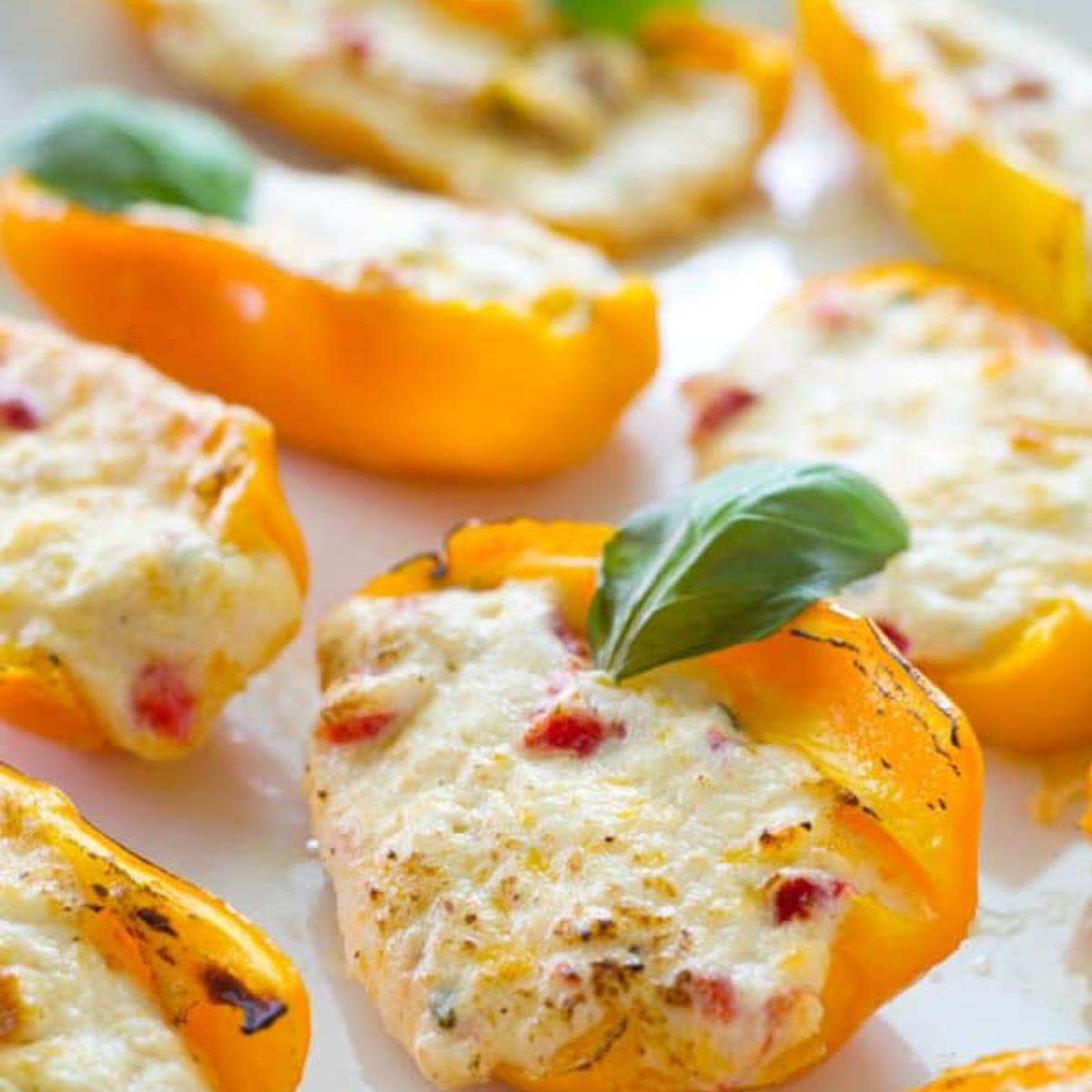  Baked mini peppers stuffed with a creamy cheese mixture, garnished with fresh basil. Served on a white platter.