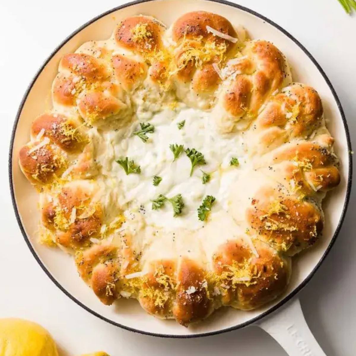 A cast iron skillet filled with a creamy dip surrounded by golden-brown bread rolls.