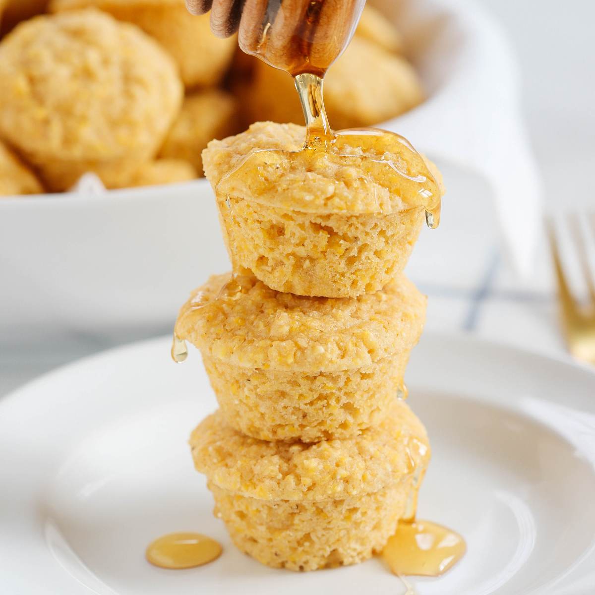 A stack of three mini cornbread muffins, with honey dripping from the top.