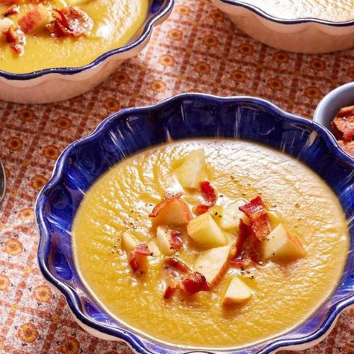 A bowl of creamy apple soup topped with crispy bacon and diced apples.