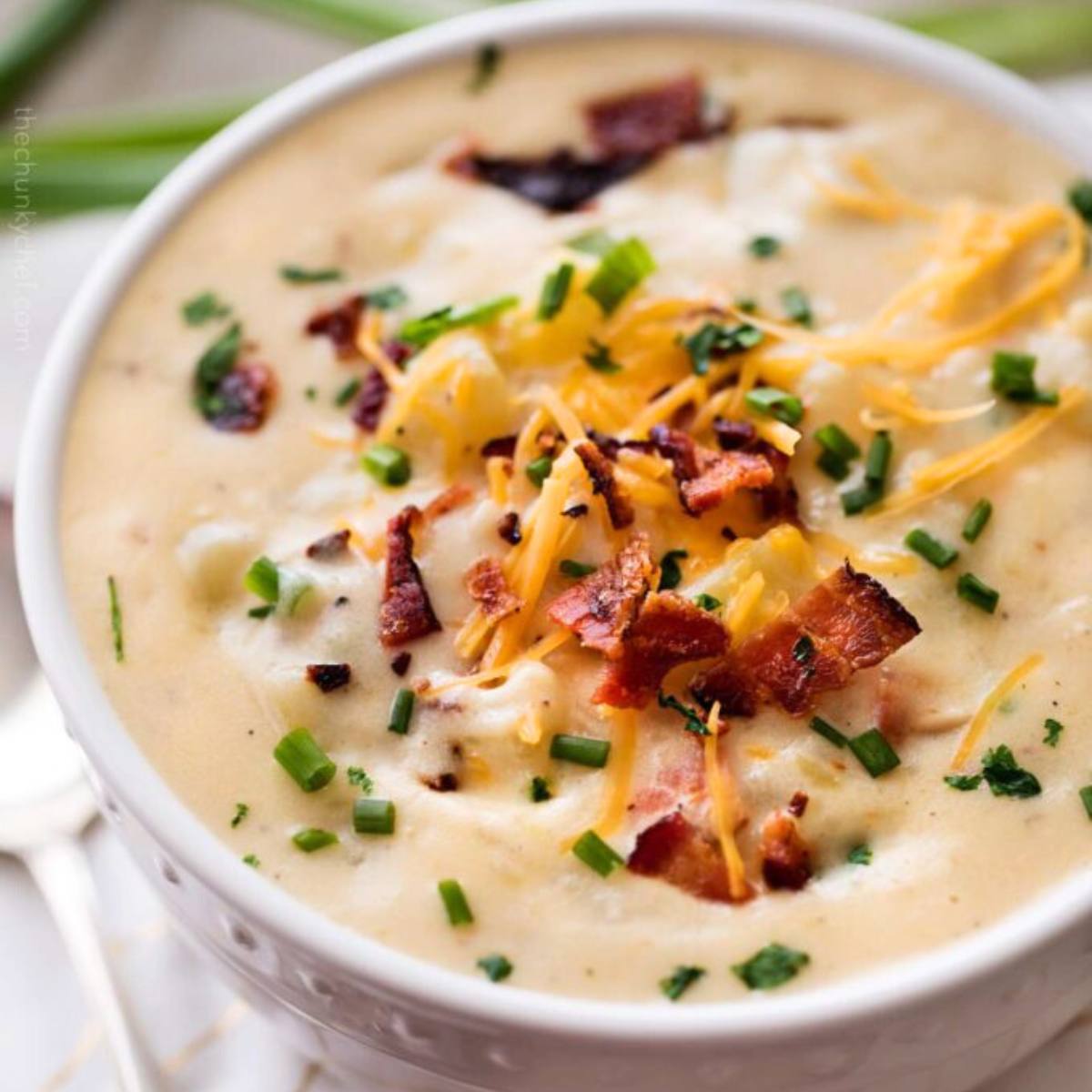 A bowl of creamy potato soup topped with bacon bits, shredded cheese, and chives.