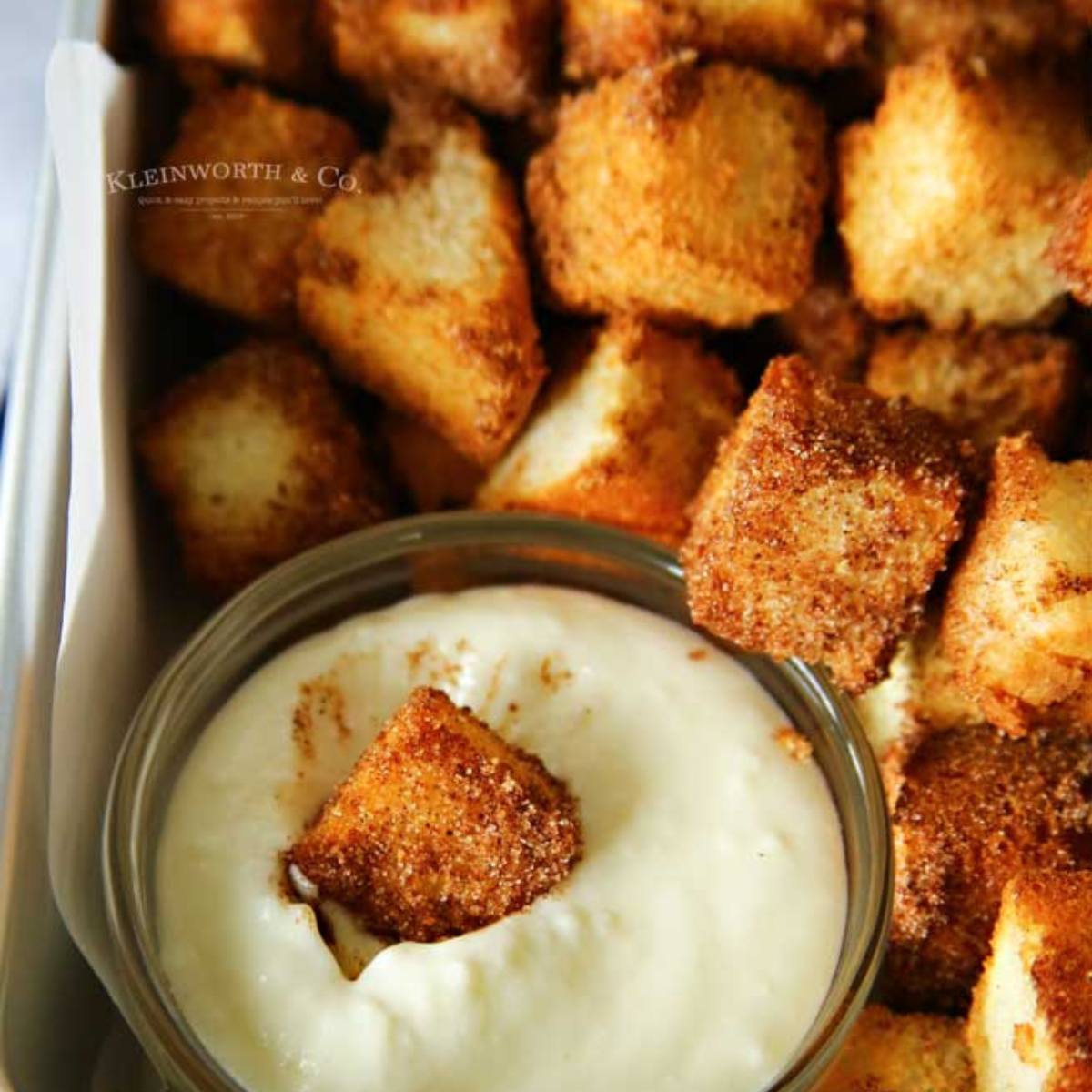 A close-up of a bowl of cinnamon sugar croutons being dipped into a bowl of creamy dip.