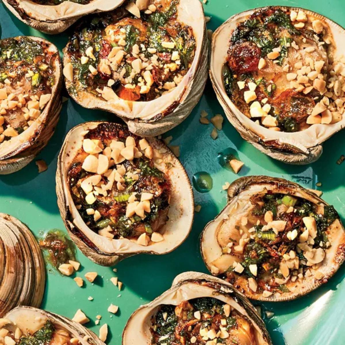 A plate of grilled clams topped with a spicy peanut sauce and chopped peanuts.