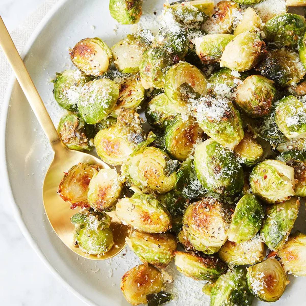 A plate of roasted Brussels sprouts with Parmesan cheese and a golden spoon.