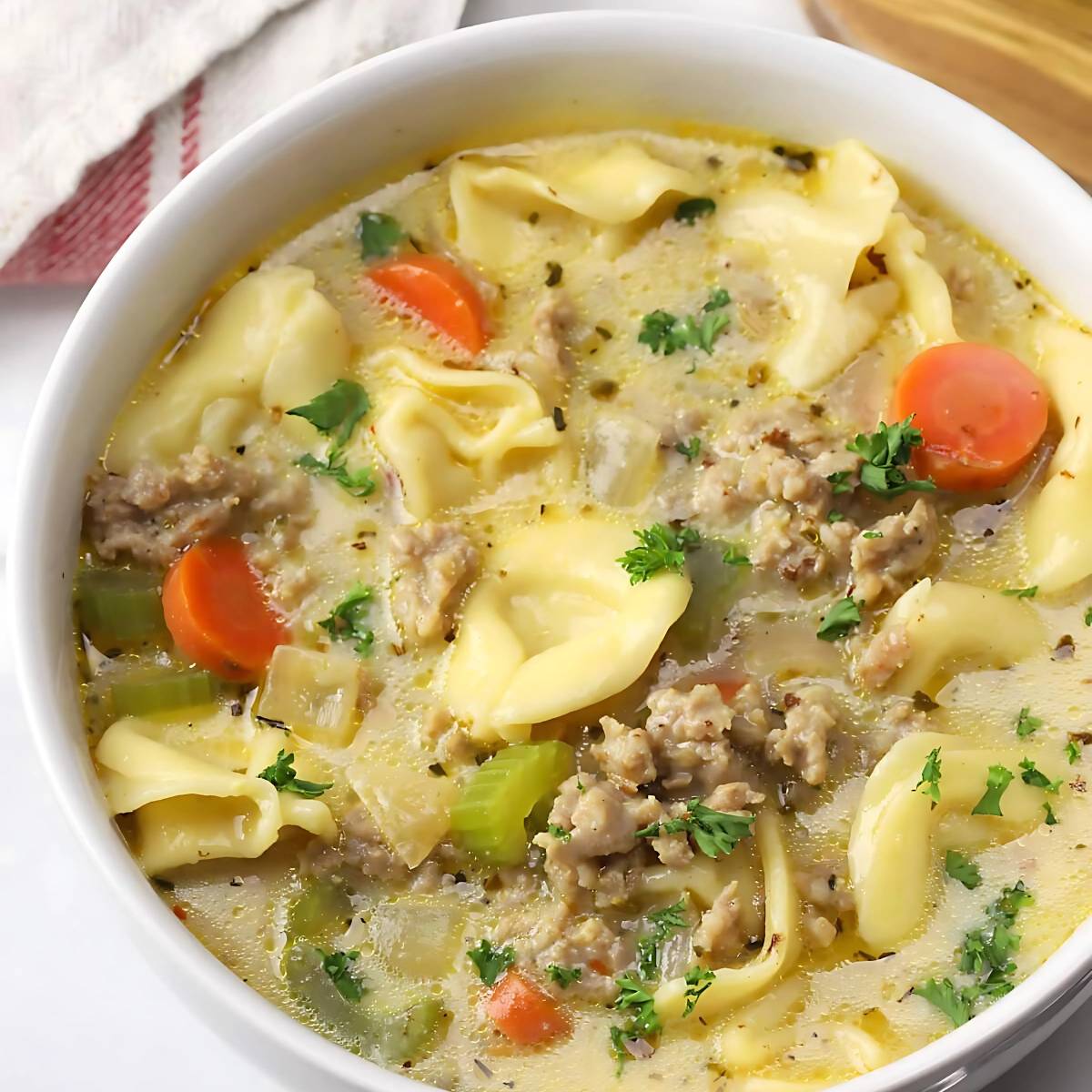 A close-up shot of a white bowl filled with a comforting tortellini soup, ready to be enjoyed.