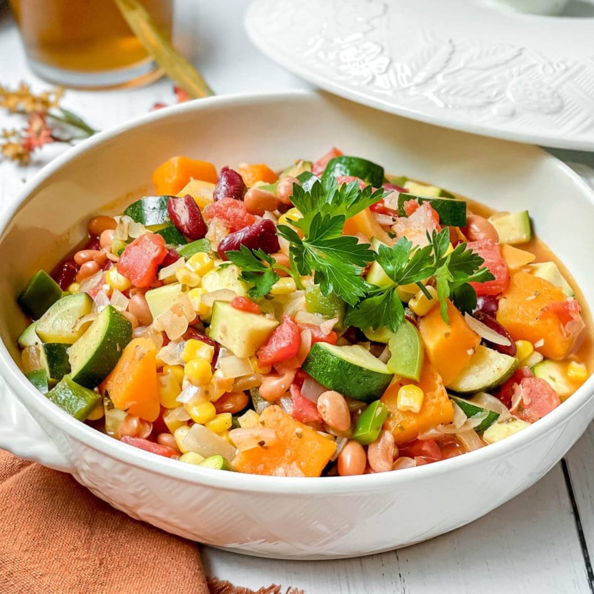 A bowl of hearty vegetable chili with beans, corn, zucchini, and squash.