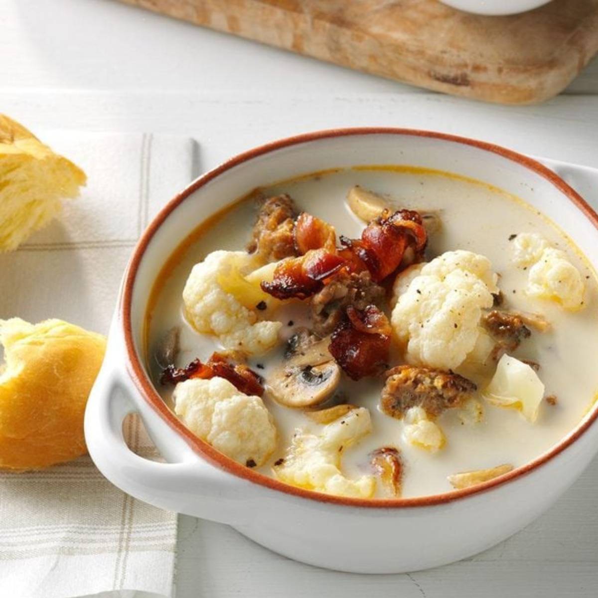 A bowl of creamy cauliflower soup topped with crispy bacon, sausage, and mushrooms.