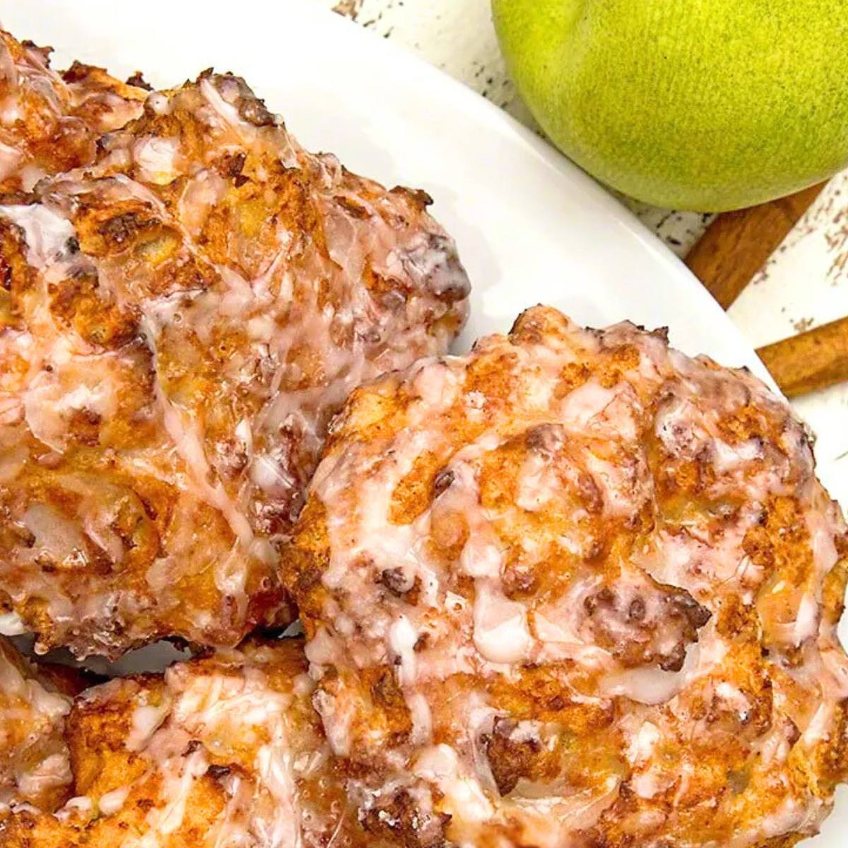 A close-up of a plate of golden-brown apple fritters drizzled with glaze.